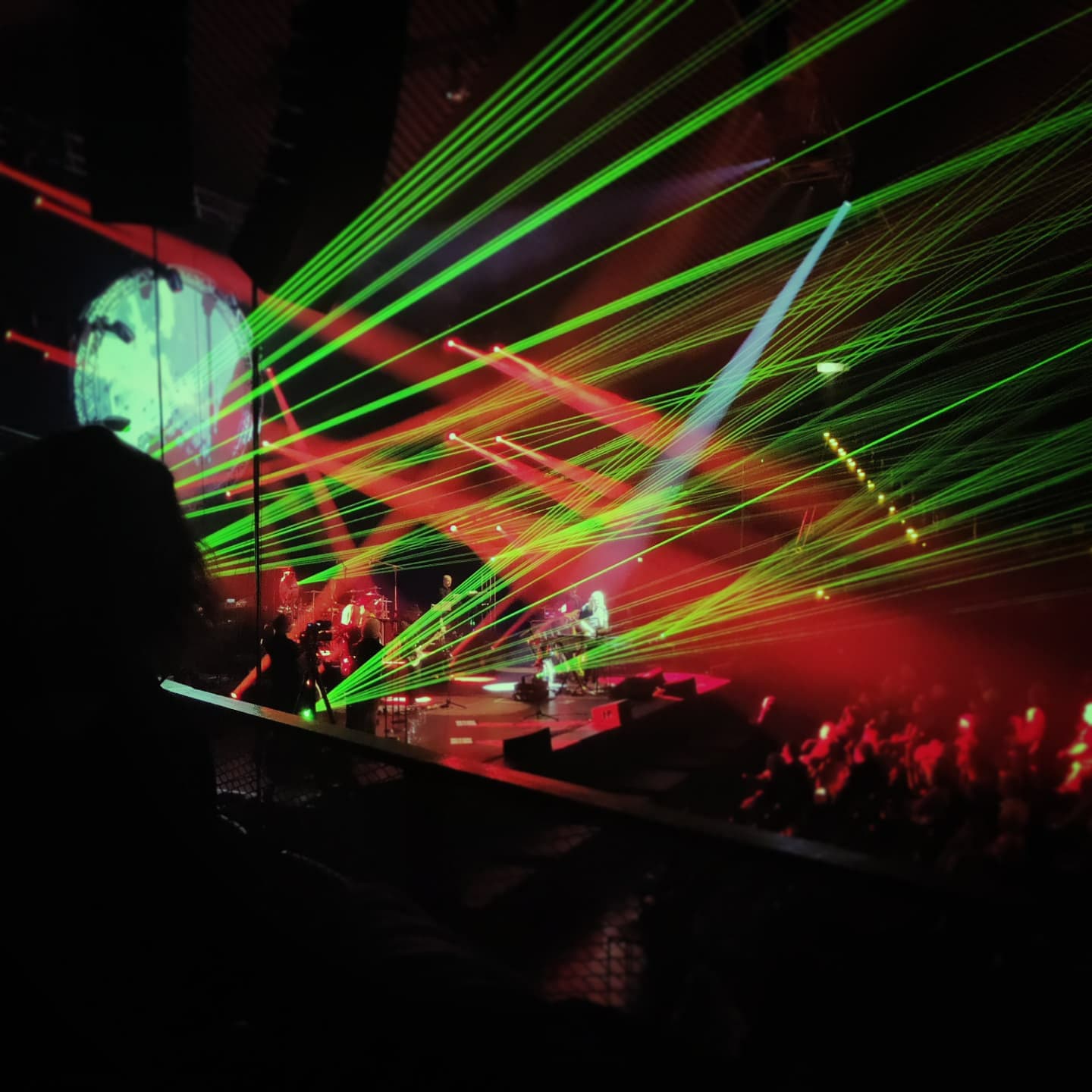 photo of a light show at a concert, with lots of green beams eminating from the stage at the left side, shooting towards the top right of the image. there's also some red lights shining towards the crowd